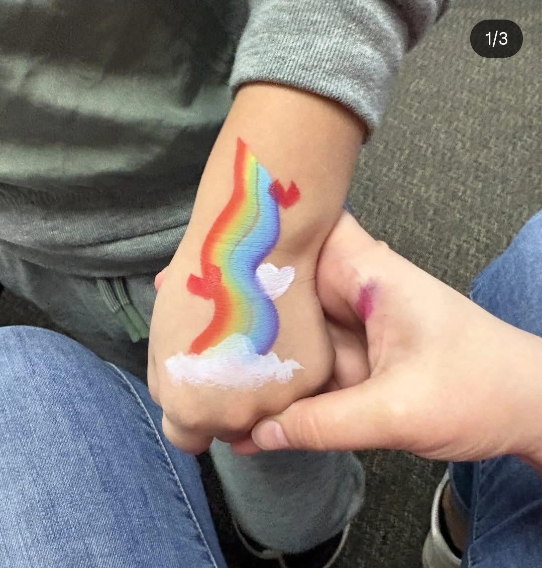 Rainbow rising from a white cloud painted on the back of a child's hand